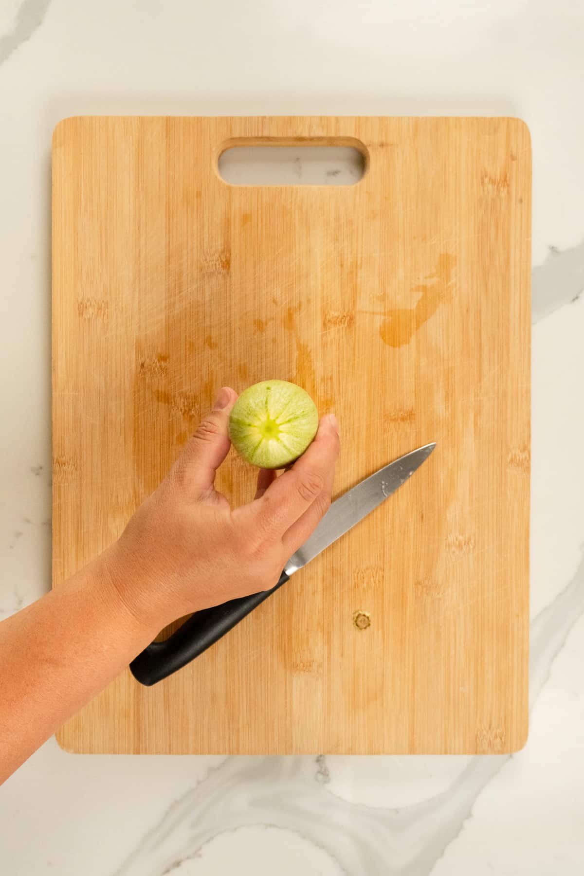 a hand holding a trimmed zucchini bottom on a chopping board and knife
