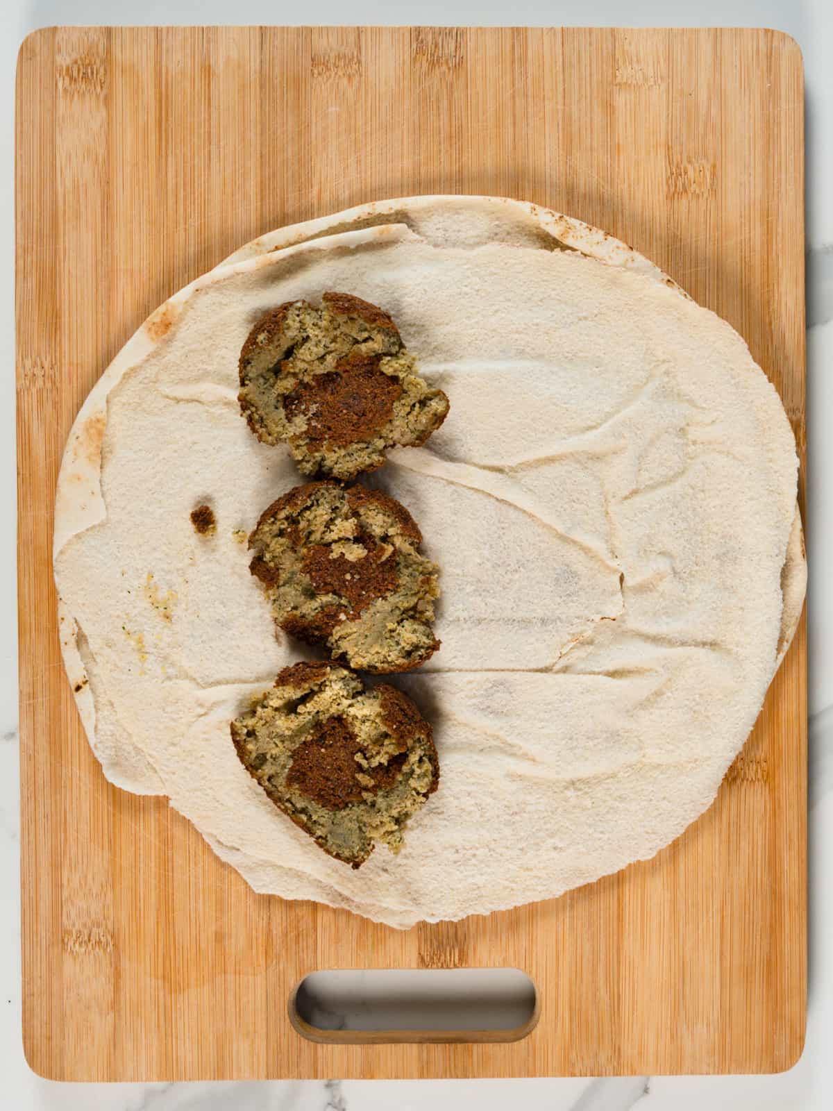3 squashed falafel balls in a flat round pita bread
