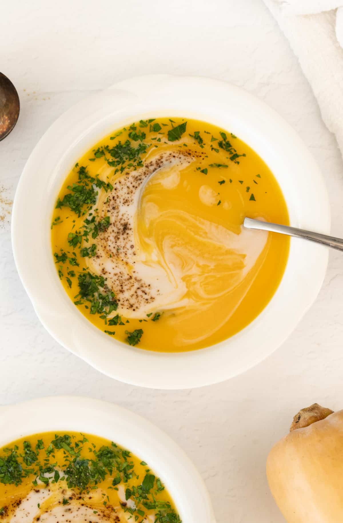 a bowl with orange butternut soup garnished with fresh parsley flakes and coconut milk