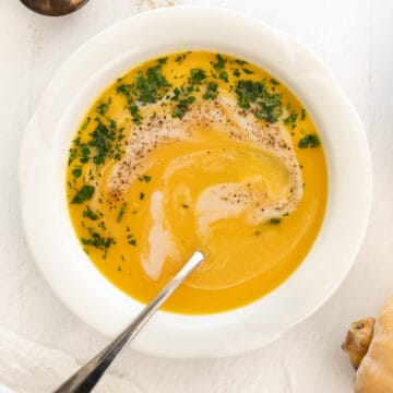 a white bowl of vegan butternut squash soup with coconut milk drizzle and parsley as garnish