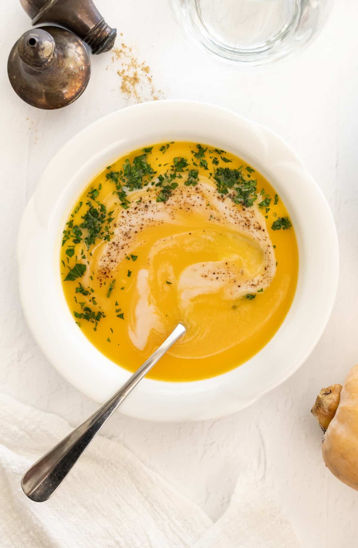 a white bowl of vegan butternut squash soup with coconut milk drizzle and parsley as garnish