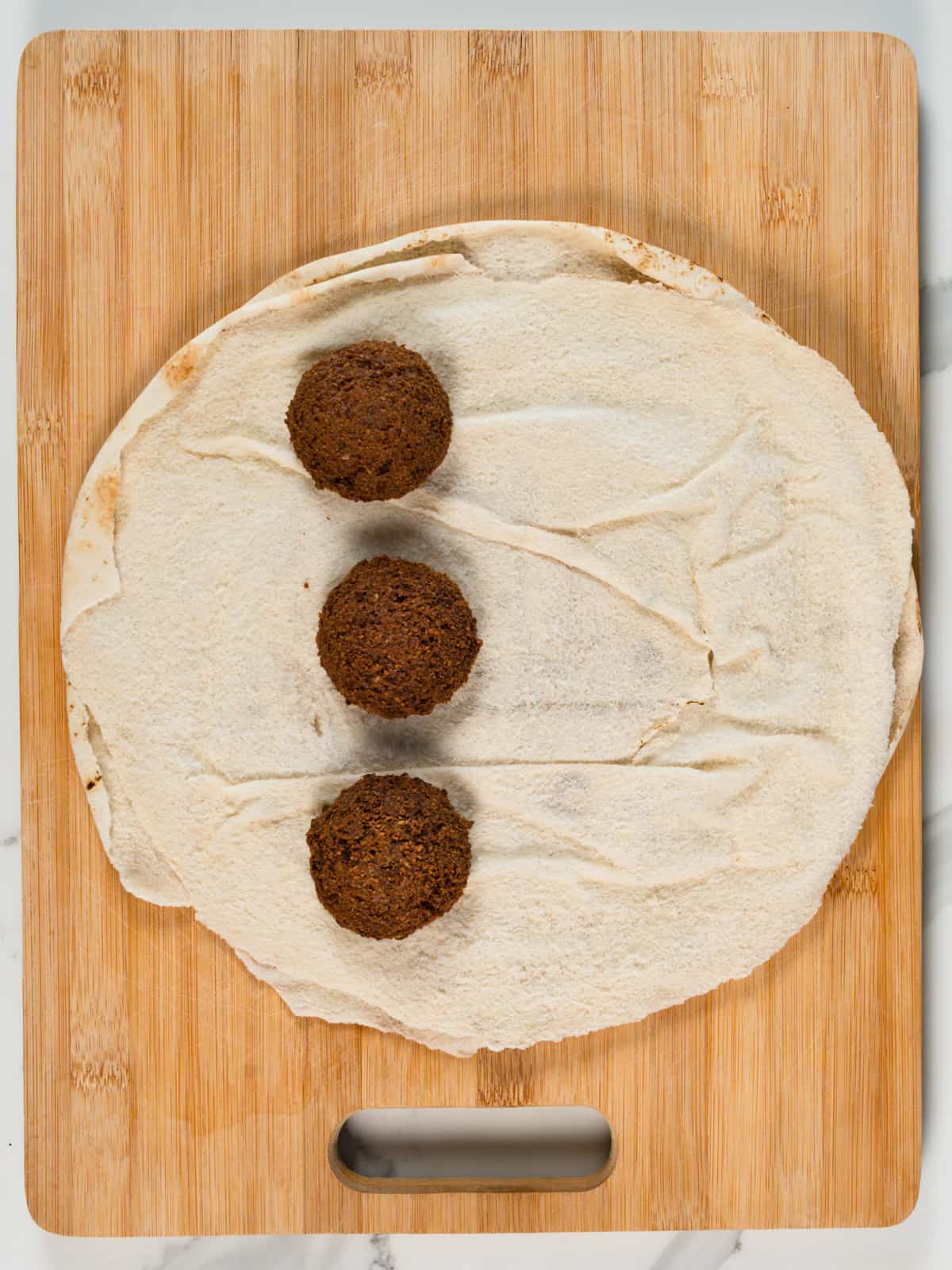 round pita bread with 3 brown falafel balls on a wood chopping board