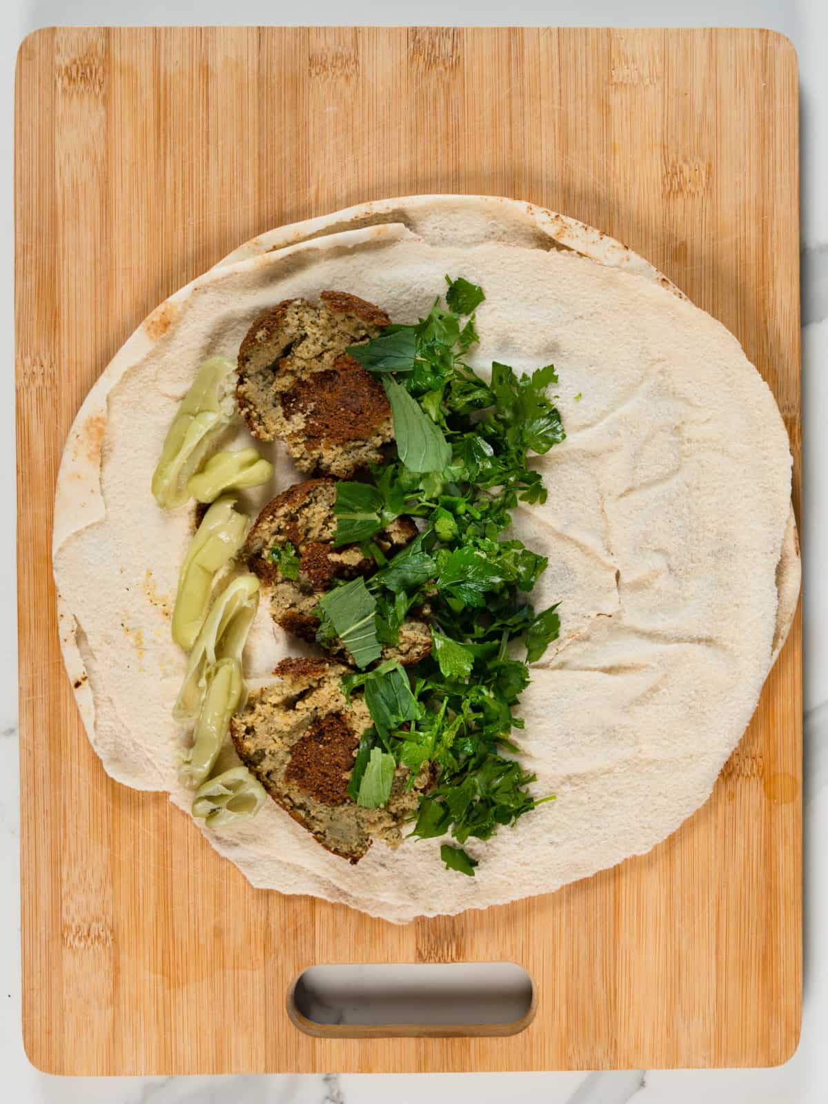 mint and parsley leaves with green pickled chillis in a round pita bread with squashed falafel