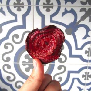 a single beetroot chip held up by a hand in front of patterned tiles