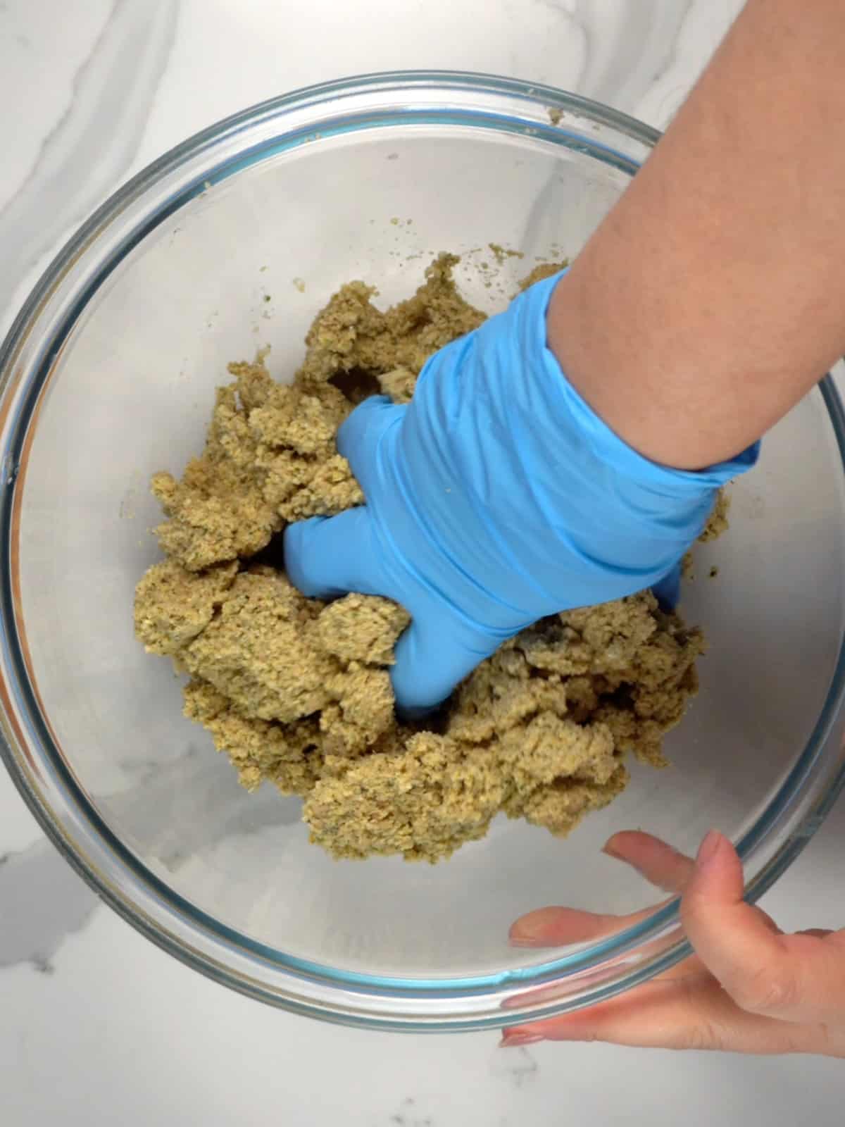a female hand with a blue glove kneading the falafel mixture