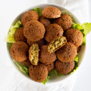 a white plate of falafel with one opened in half