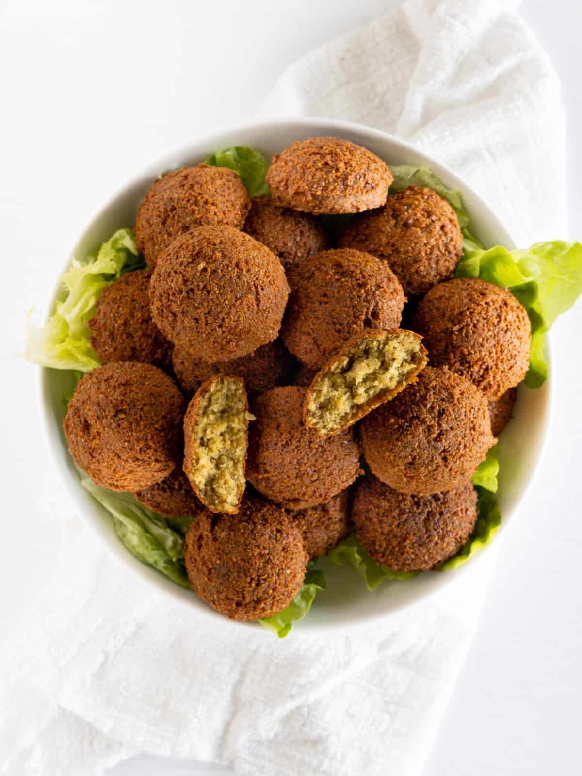 a white plate of falafel with one opened in half
