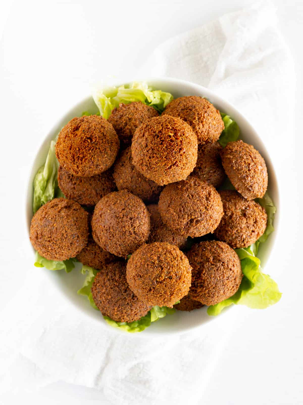 một chiếc đĩa tròn màu trắng chứa đầy những chiếc bát falafel màu nâu với rau diếp xanh bên dưới