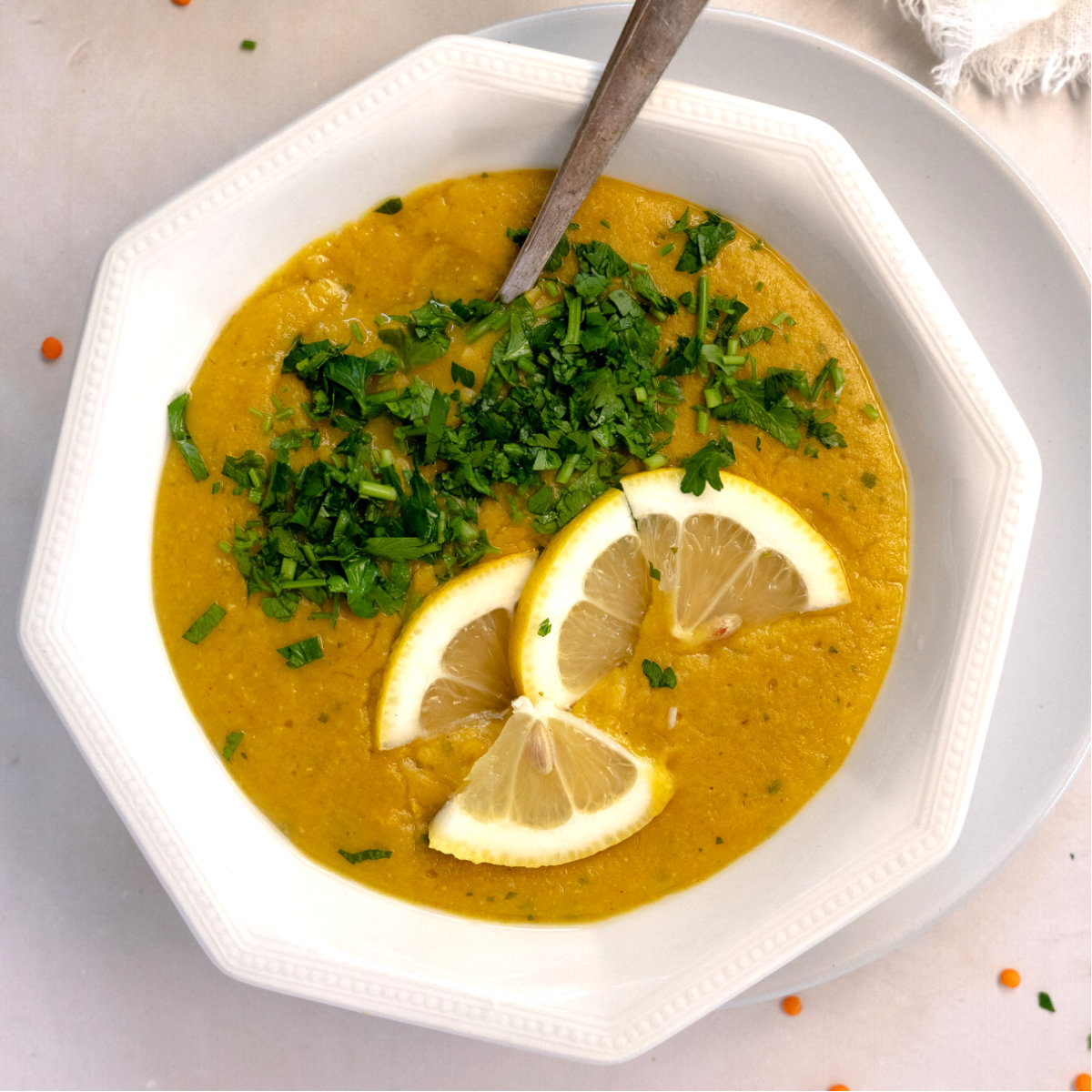 white bowl of yellow soup toped with chop parsley and slices of lemon