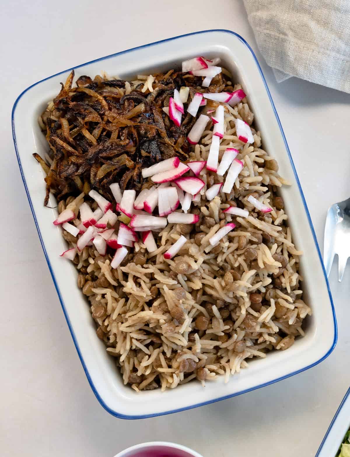 cooked lentils and rice topped with caramelized onions and chopped radish in a white plate