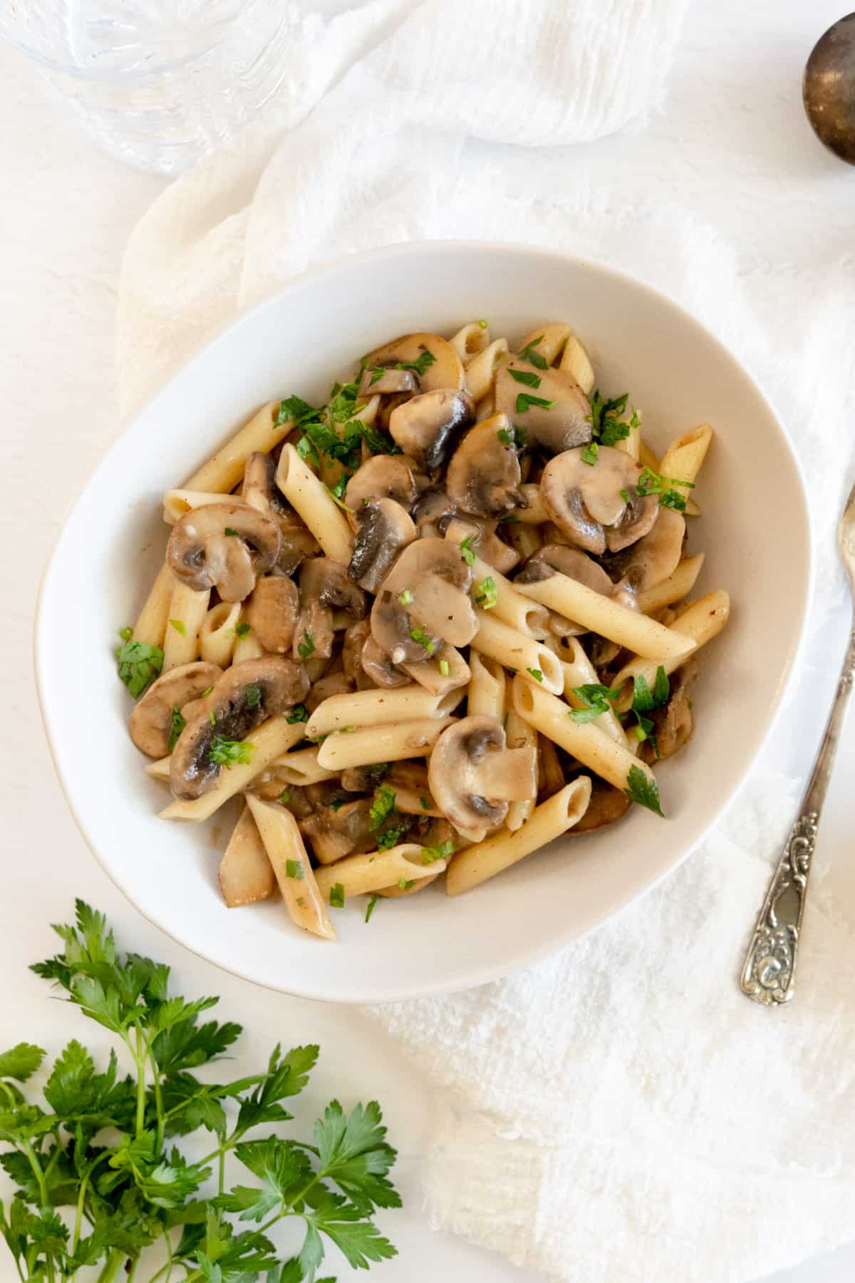 cooked penne pasta, sliced mushrooms and parsley in a bowl