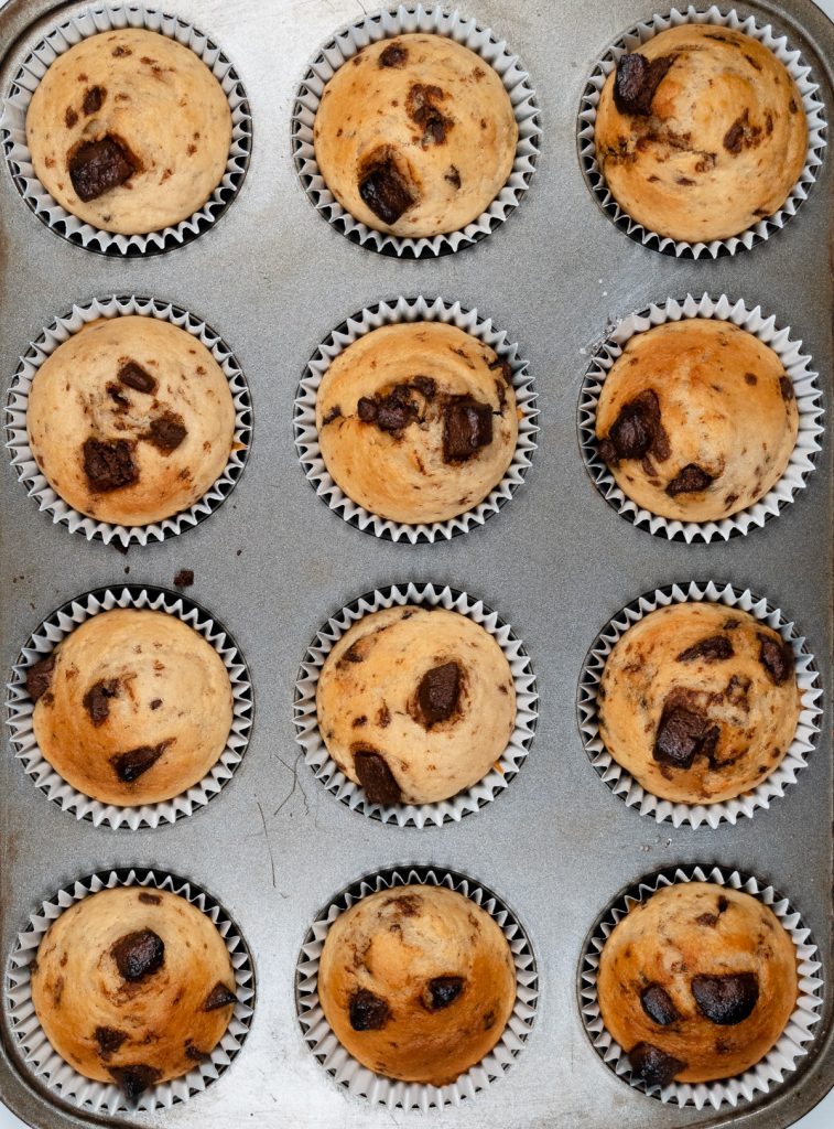 12 baked choc chip muffins in a muffin tray
