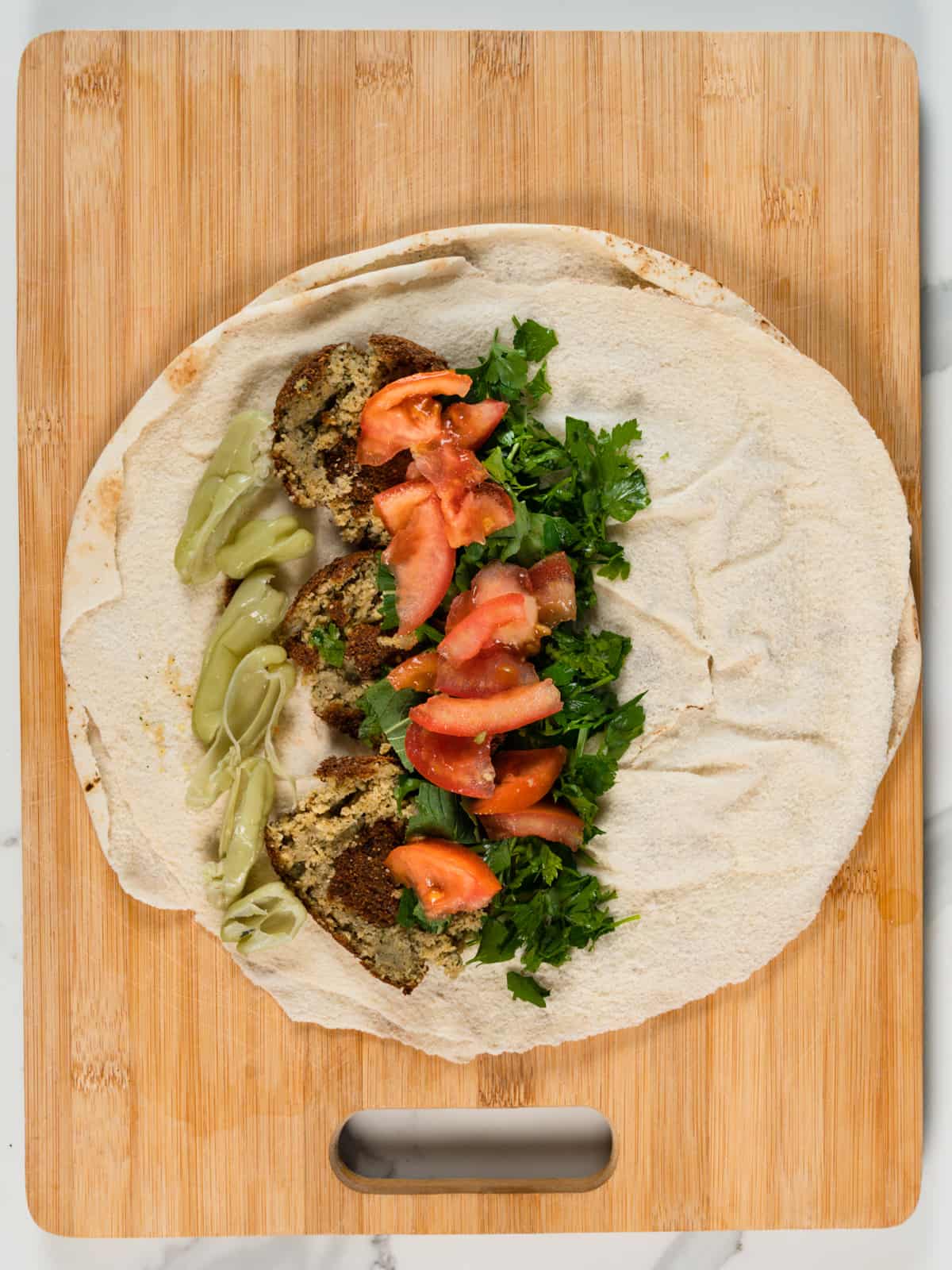 mint and parsley leaves with green pickled chillis, chopped tomatoes in a round pita bread with squashed falafel