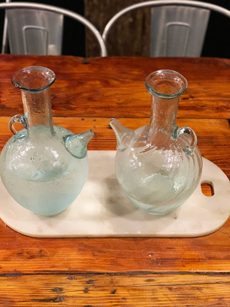 Two Arabian water jugs full of water sitting on a marble platter on a timber table.