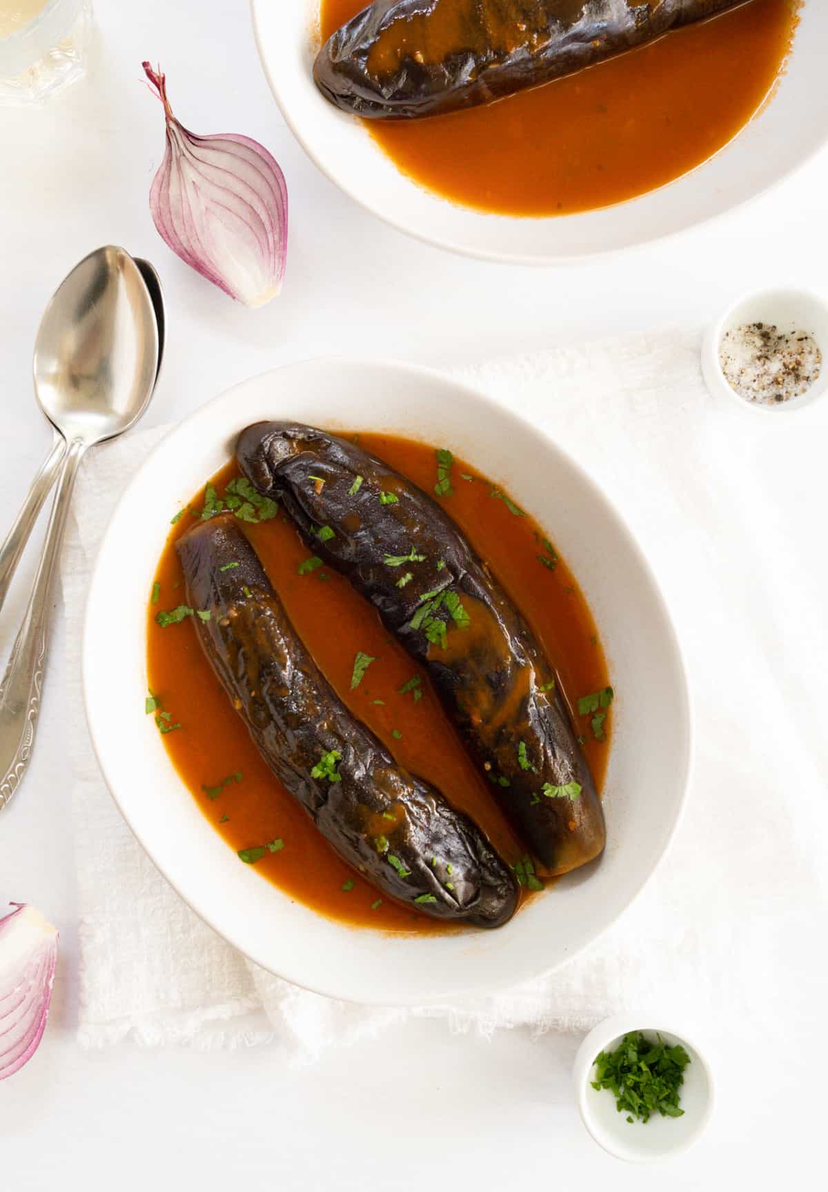 two white plates with cooked long eggplants in a red sauce
