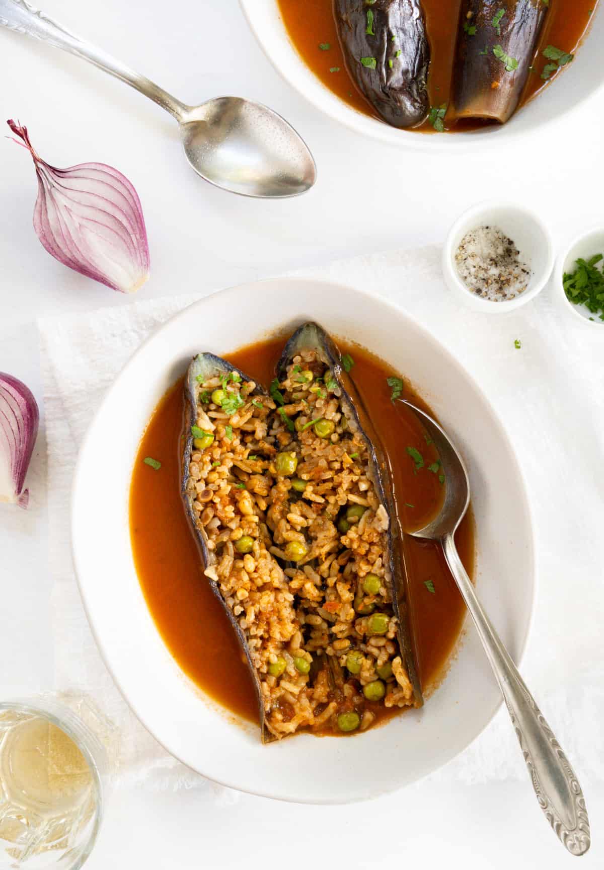 a white plate with a cooked eggplant split open to show its rice and vegetable filling in a red sauce