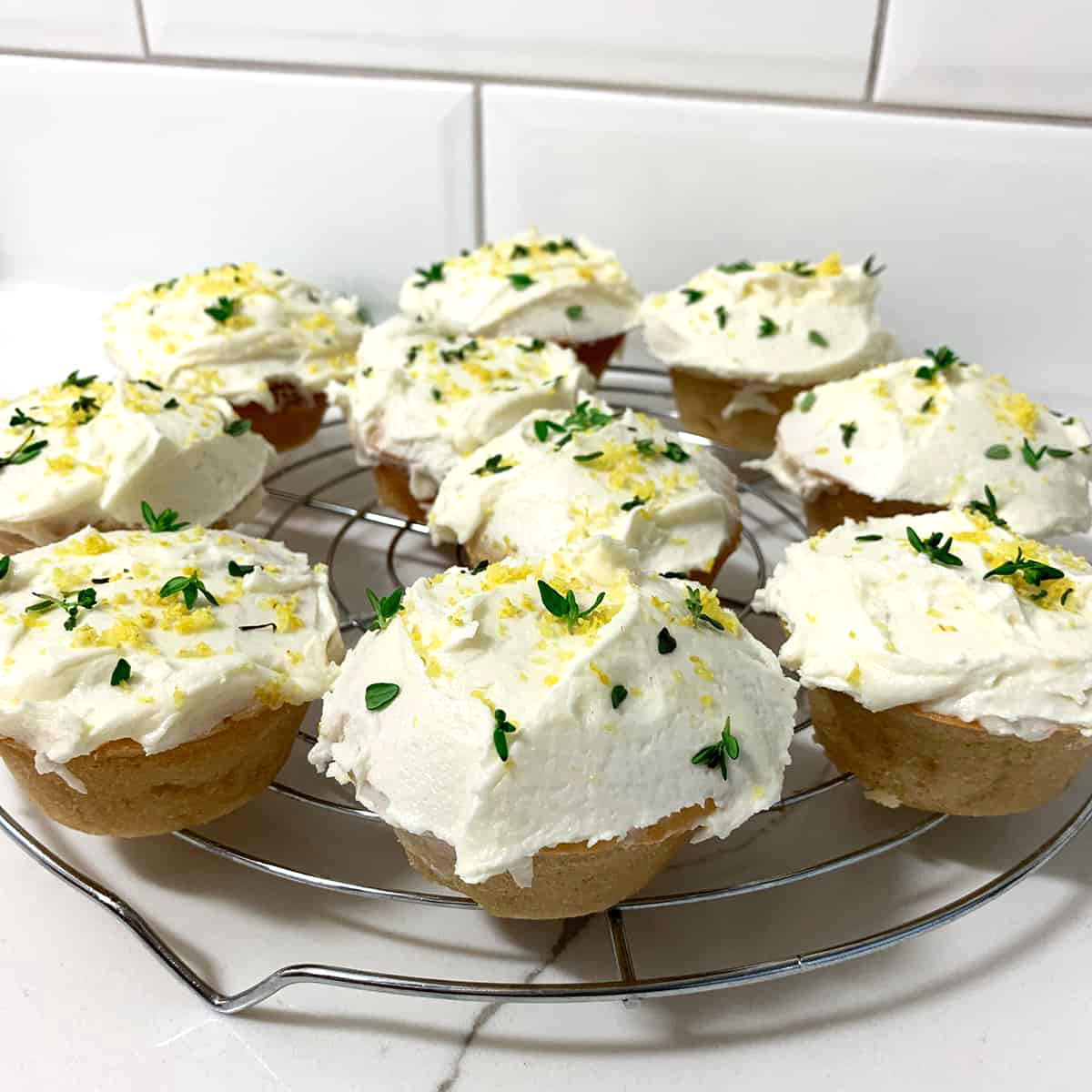 cup cakes with white frosting, lemon zest and thyme on top