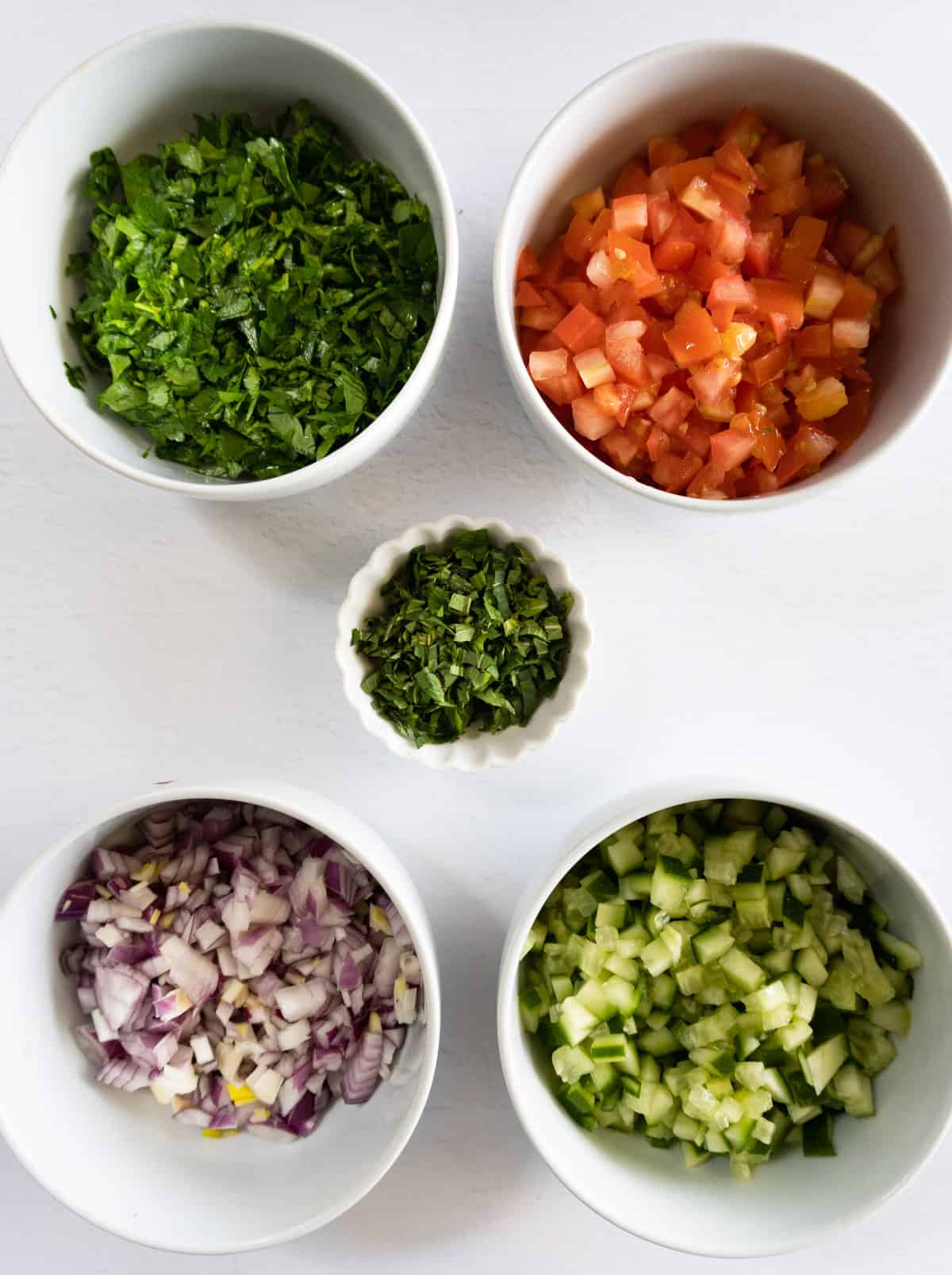 tomato, parsley, onion, mint leaves and cucumber all finely chopped in white bowls