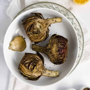 three roasted artichokes in a white plate