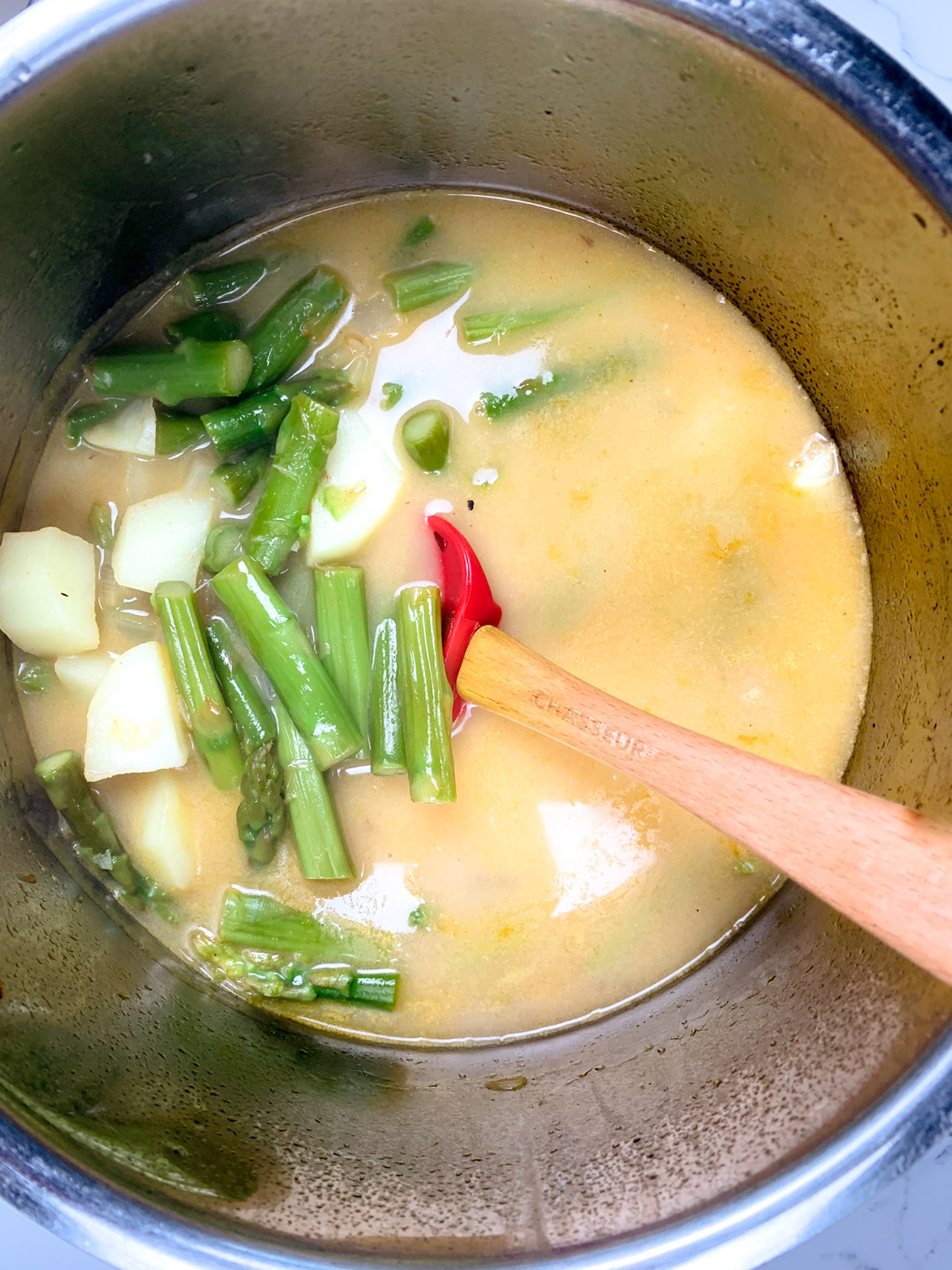 inside the pot looking at yellowish  soup with chopped asparagus and potatoes