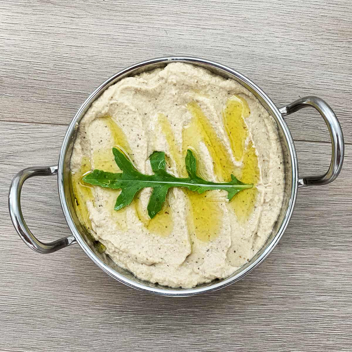 a metal plate with a yellowish dip and a green leaf covered in oil on top