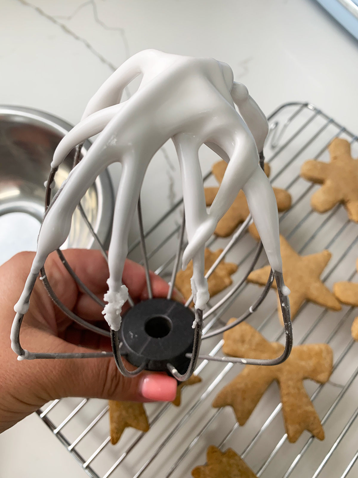 Vegan royal icing held on a whisk with gluten free gingerbread cookies in the background