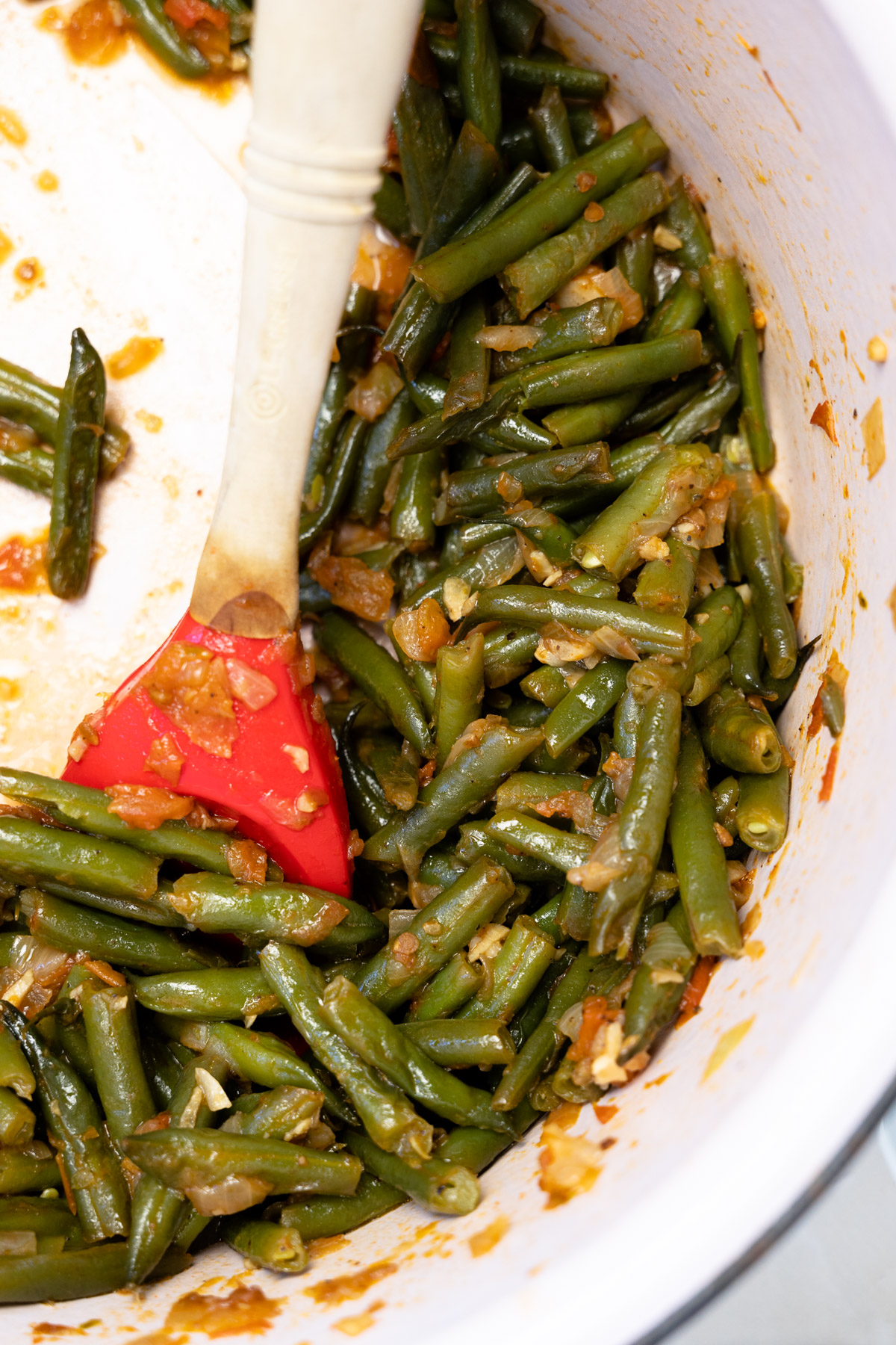close up lebanese green beans that are braised with a red silicone spoon