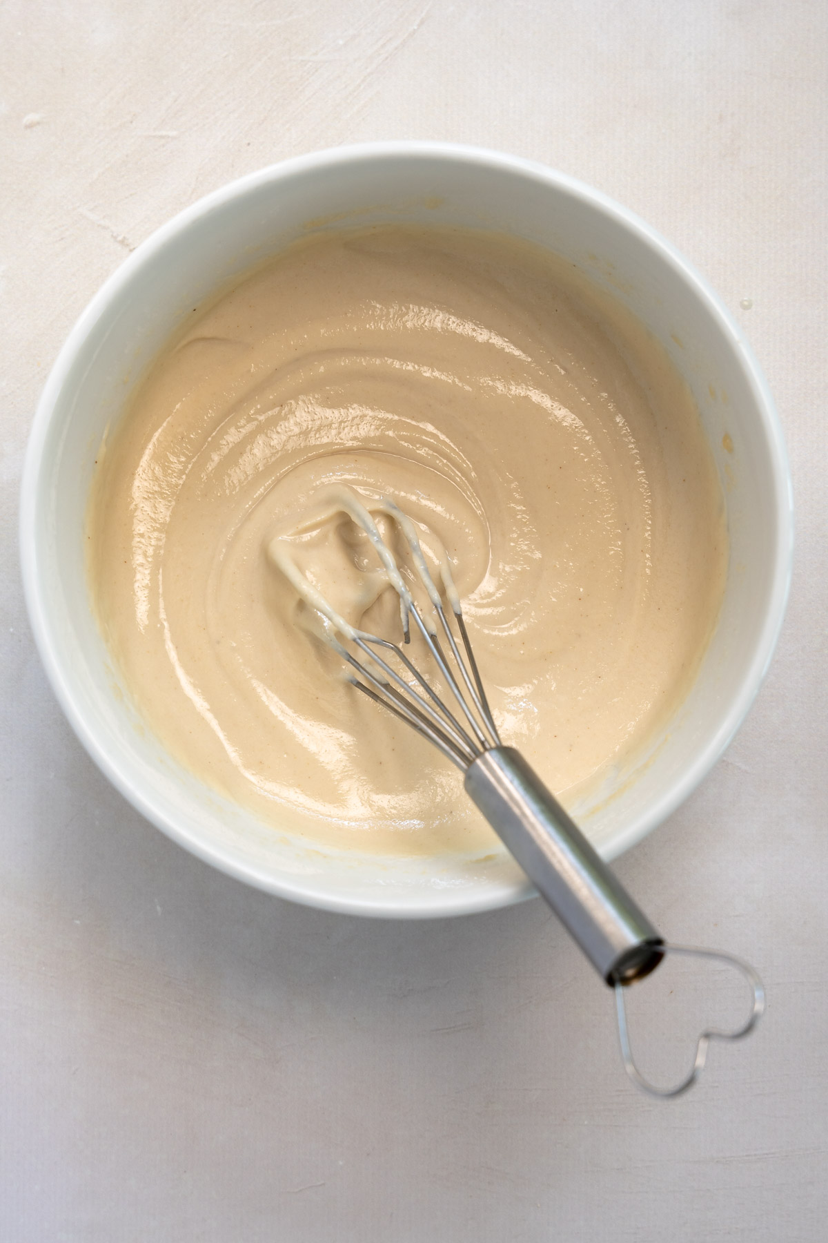 whisked tahini sauce in a white bowl with a whisk in it