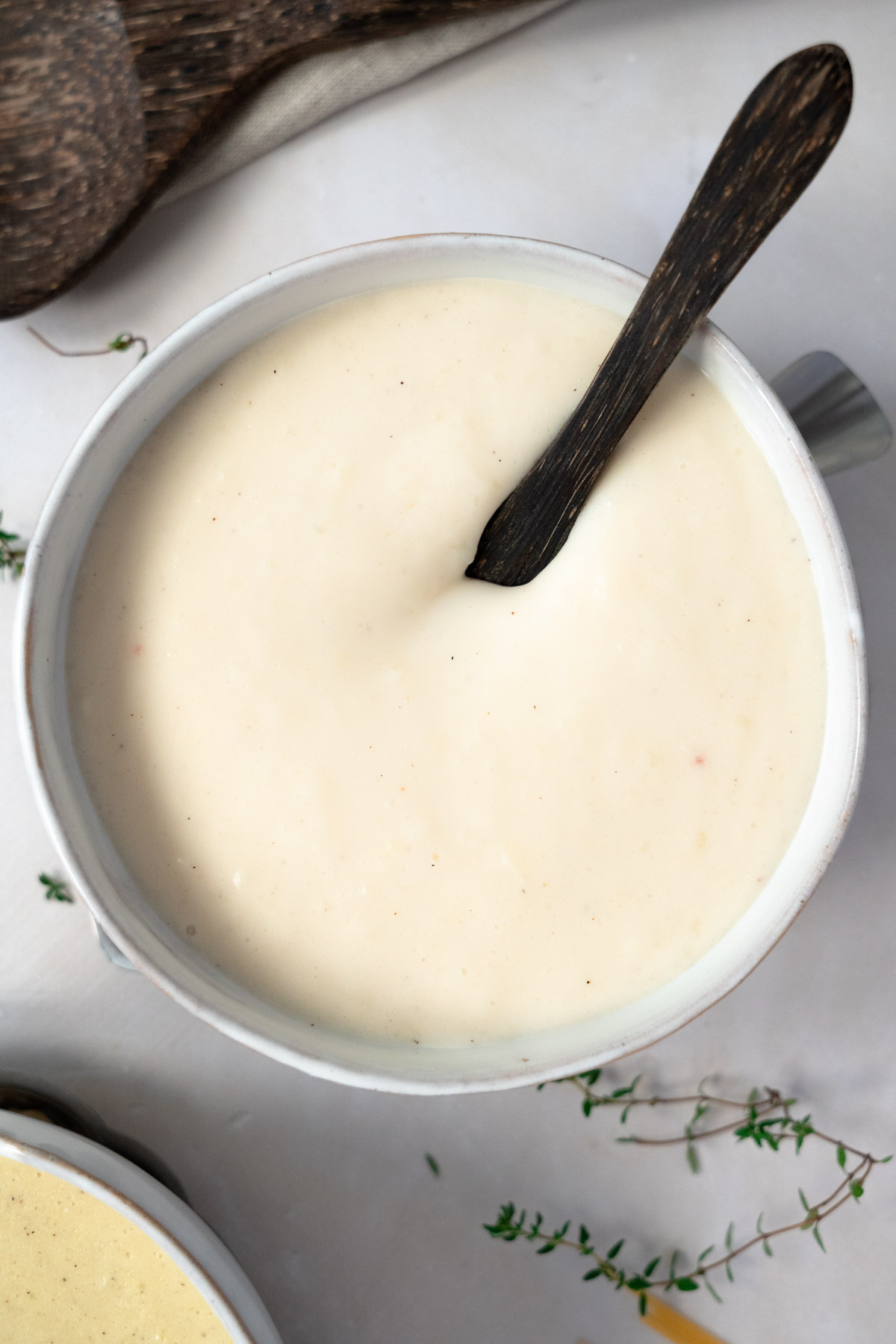 gluten free vegan bechamel sauce in a white bowl with a wooden spoon dipped into it