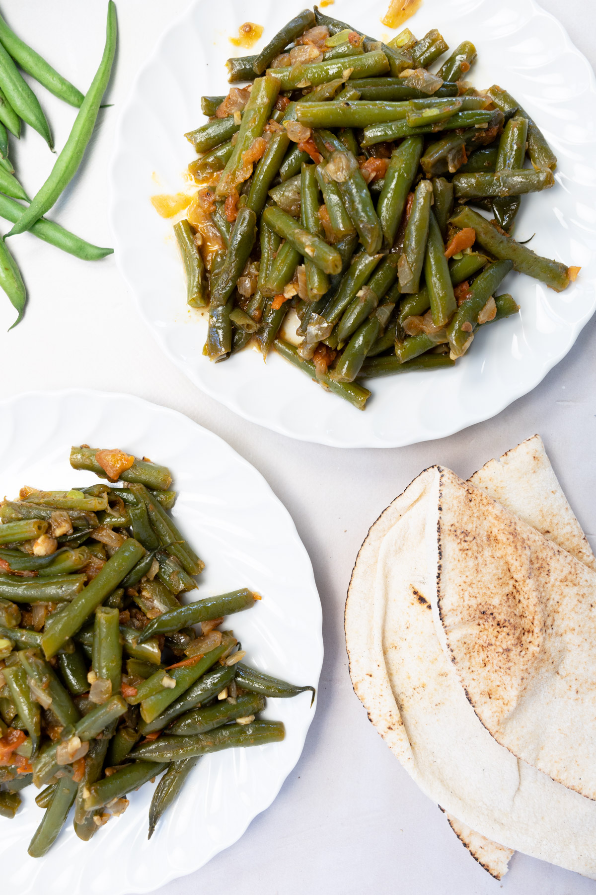 two white plates with braised green beans and a side of Lebanese bread