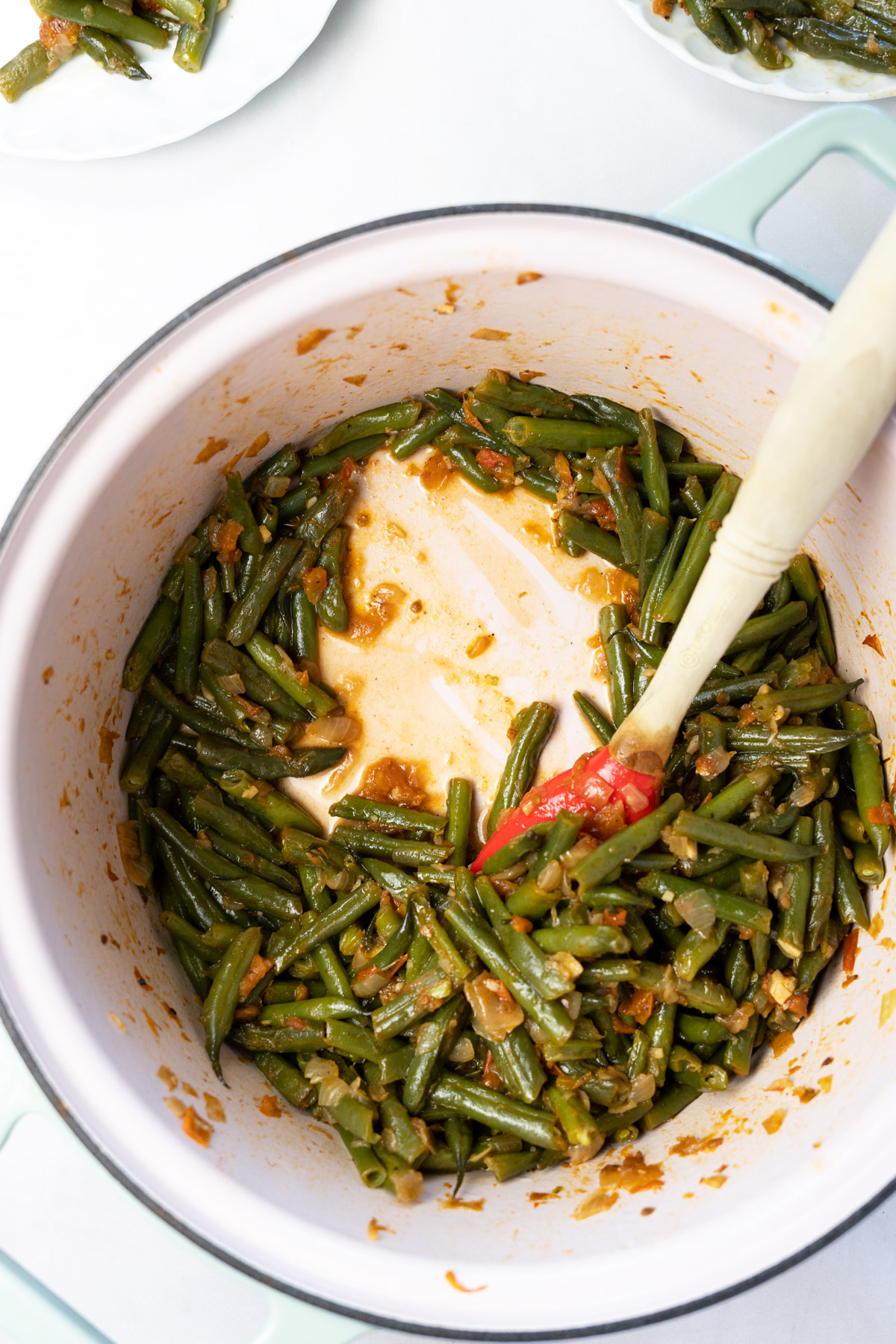 loubia braised green beans in a large pot with a red silicone spoon