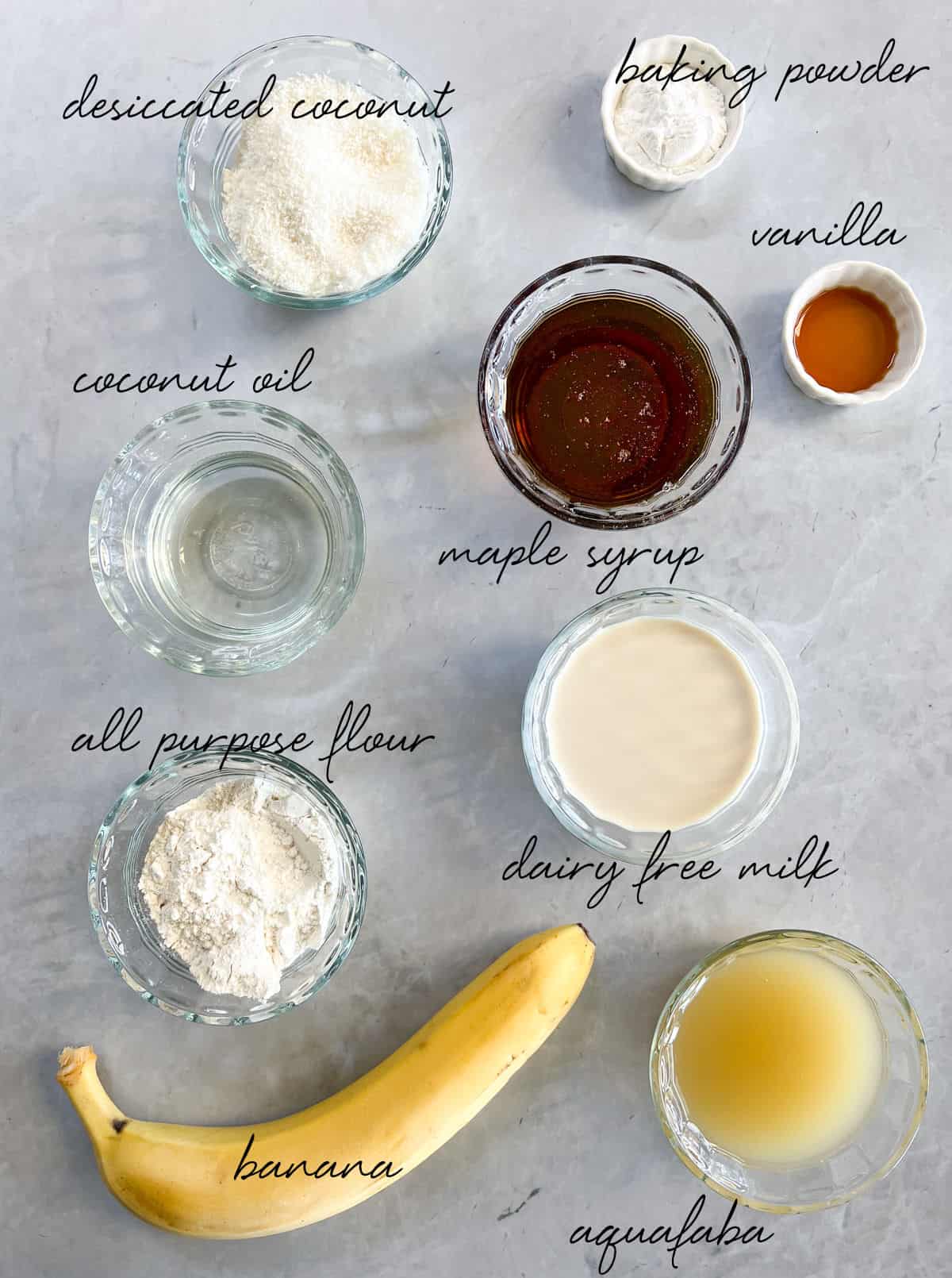 flours, milk, clear oil, a banana, yellowish liquid in bowls laid out on a grey bench