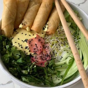 a bowl full of various greens, pickled radish and spring rolls