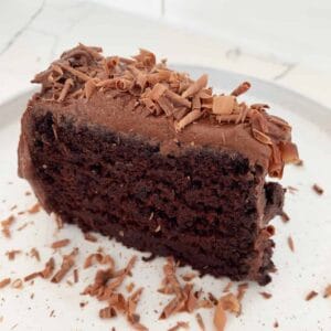 a slice of moist brown cake with chocolate icing and shavings