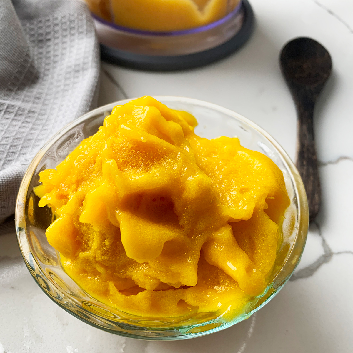 Mango Sorbet with no added sugar in a glass bowl and a wooden spoon on a white countertop