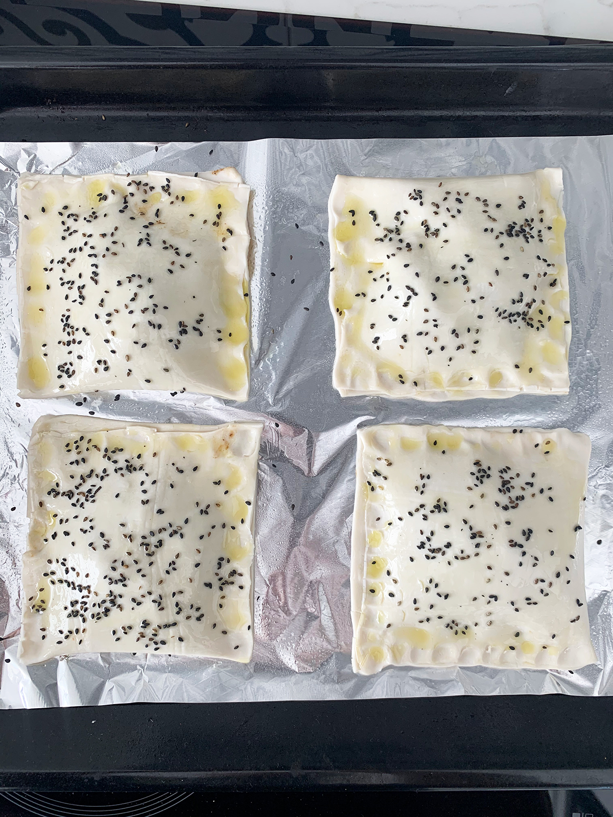 Purslane pockets smeared with olive oil and sprinkles of black sesame on baking tray ready for baking