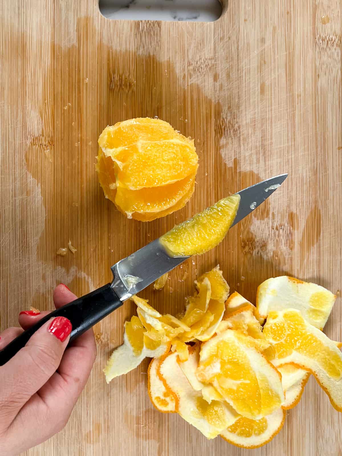 a female hand holding a knife with an orange segment next to a peeled orange