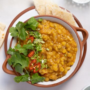 a white bowl of cooked yellow split pea with roti on the side