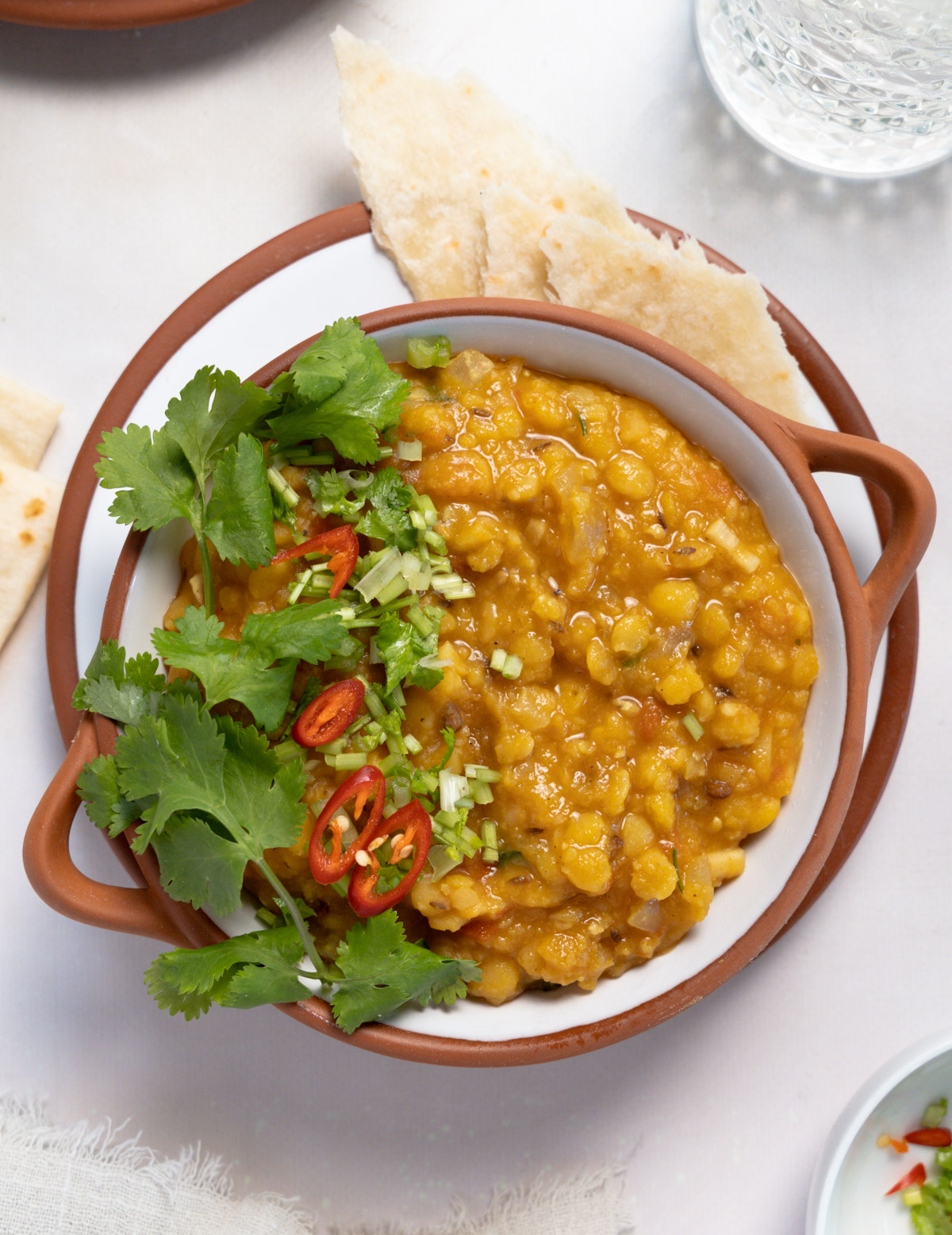 a white bowl of cooked yellow split pea with roti on the side