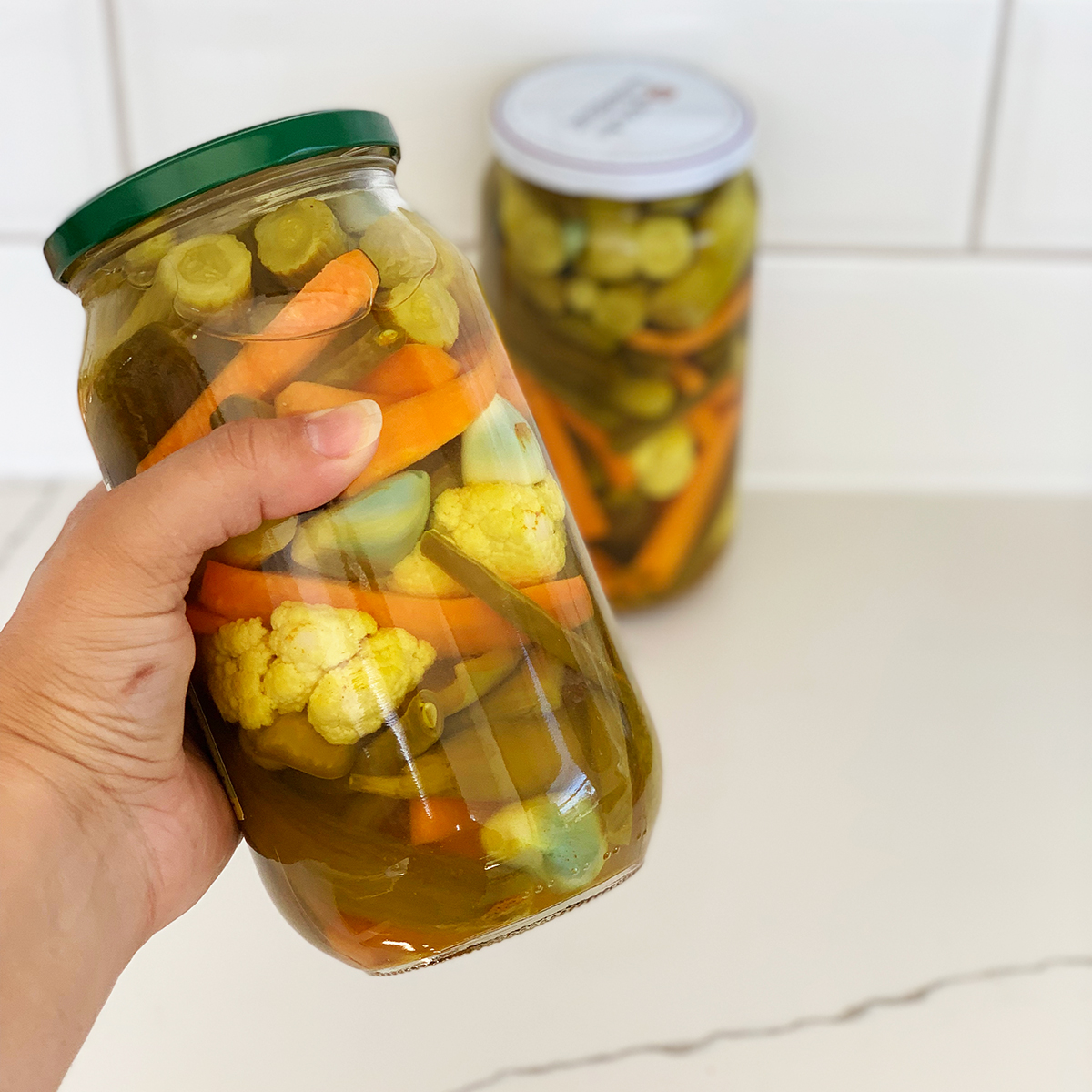 Home made pickled vegetables in two jars, one held in a hand