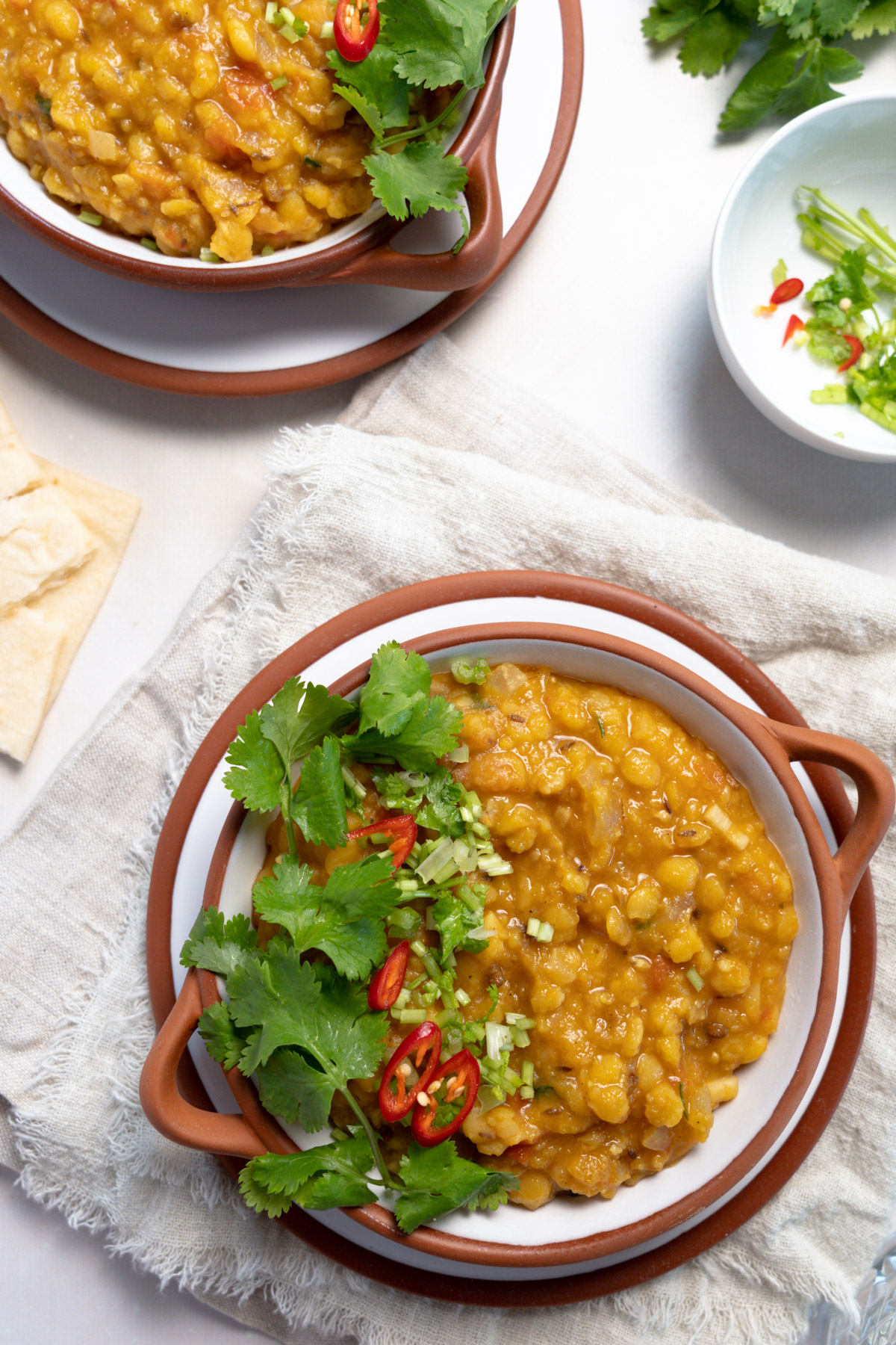 two bowls of yellow split pea dal garnished with coriander and chilli