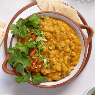 a plate of yellow dal with cilantro and red chili on top