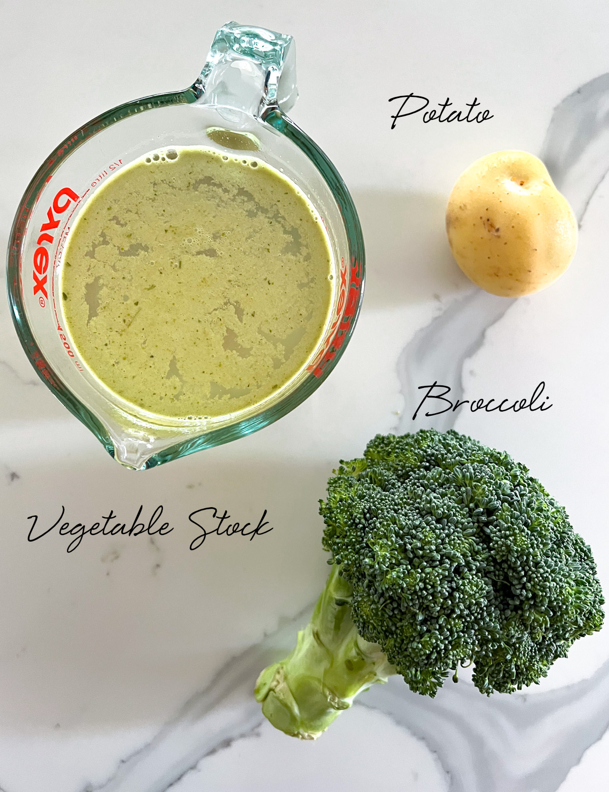 a broccoli, potato and a cup of vegetable stock on a white bench