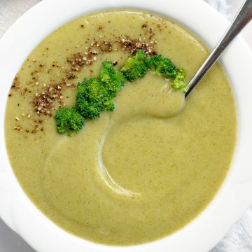 a white bowl of green broccoli soup topped with broccoli pieces and pepper