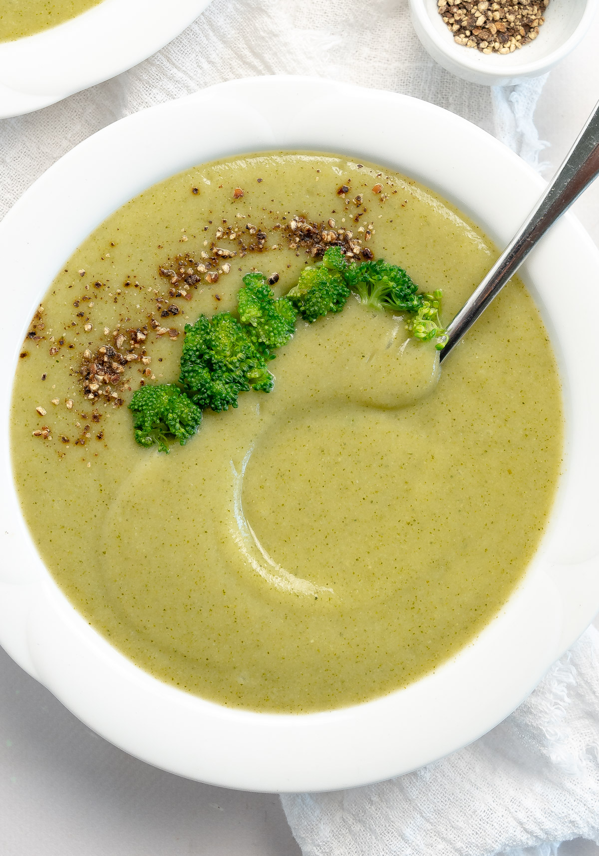 a white bowl of green broccoli soup topped with broccoli pieces and pepper