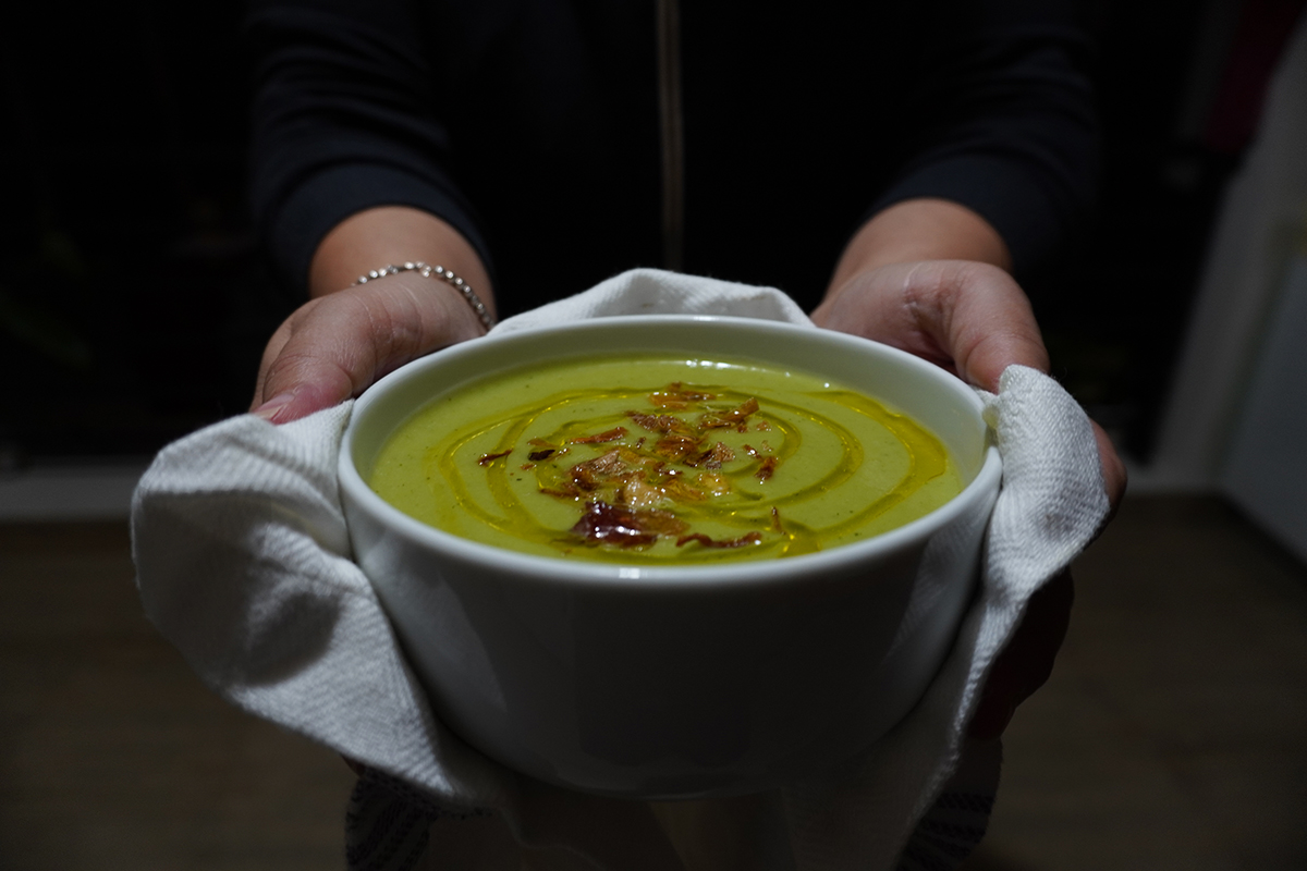 Vegan broccoli soup in a white bowl held by two hands