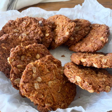 Vegan and gluten free anzac biscuits in a white plate on crumbled baking paper