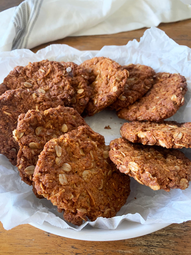Vegan and gluten free anzac biscuits in a white plate on crumbled baking paper