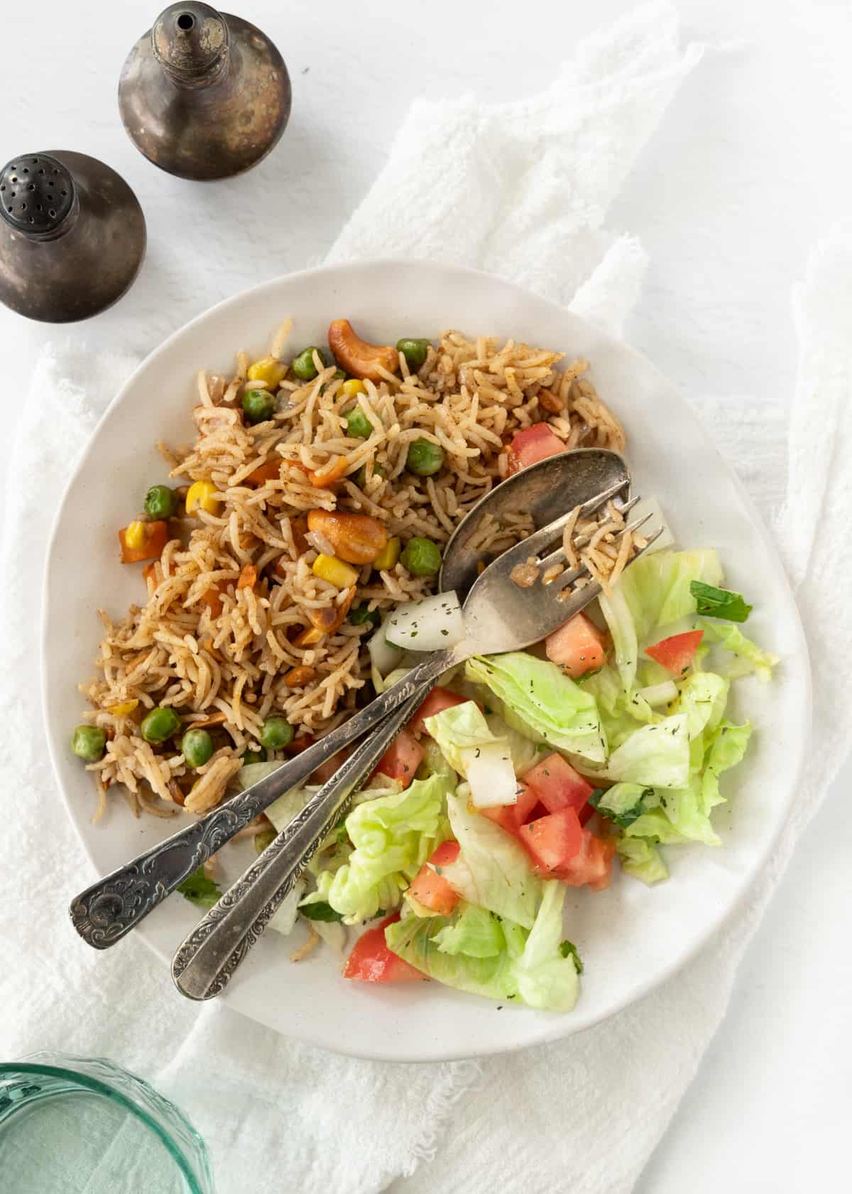a white plate with spiced rice with vegetables topped with toasted nuts and a garden salad with it