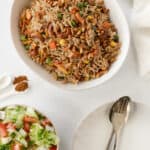 a white bowl with spiced rice with toasted nuts and vegetables and a salad on the side